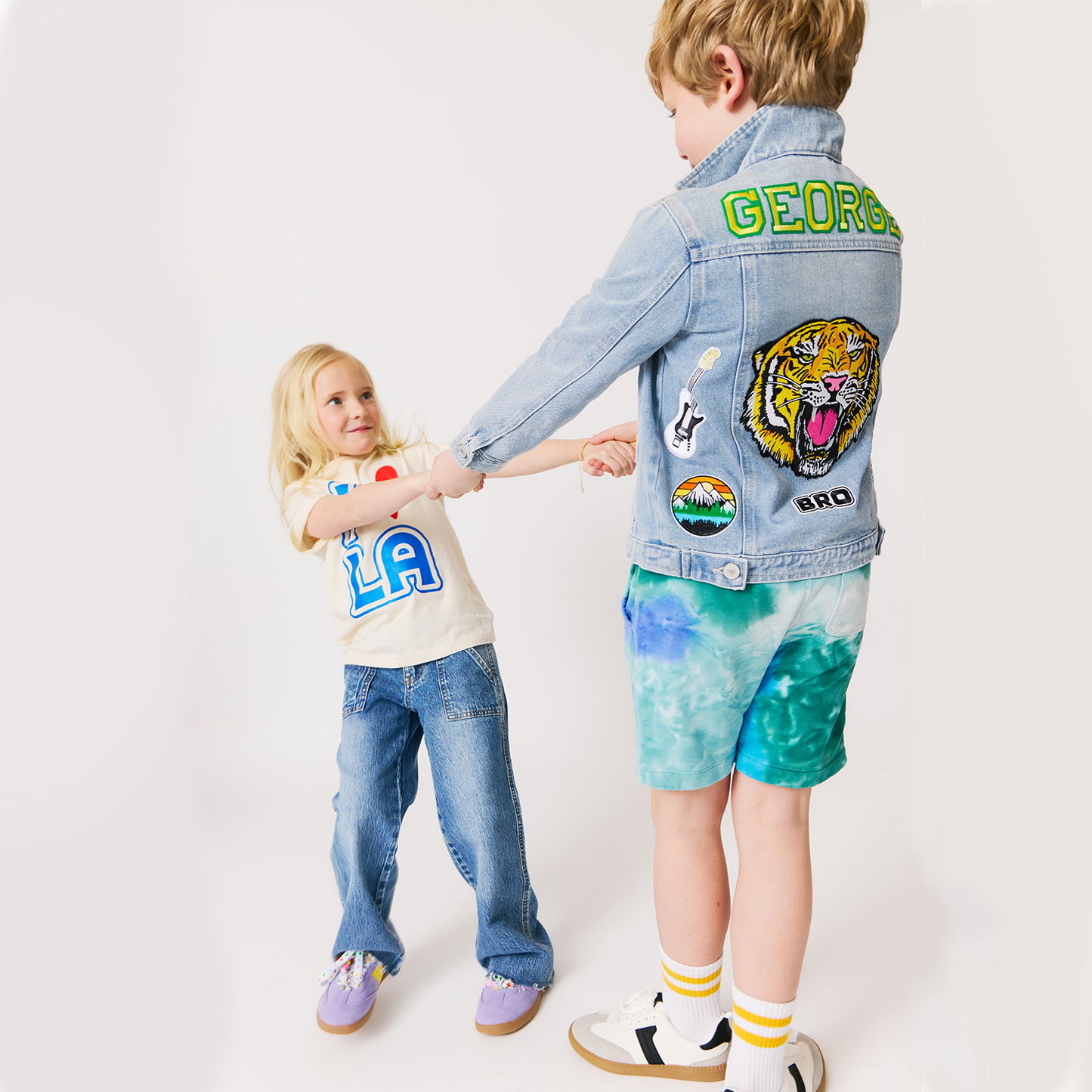 Two children wearing denim jcustom ackets with patches on a white background