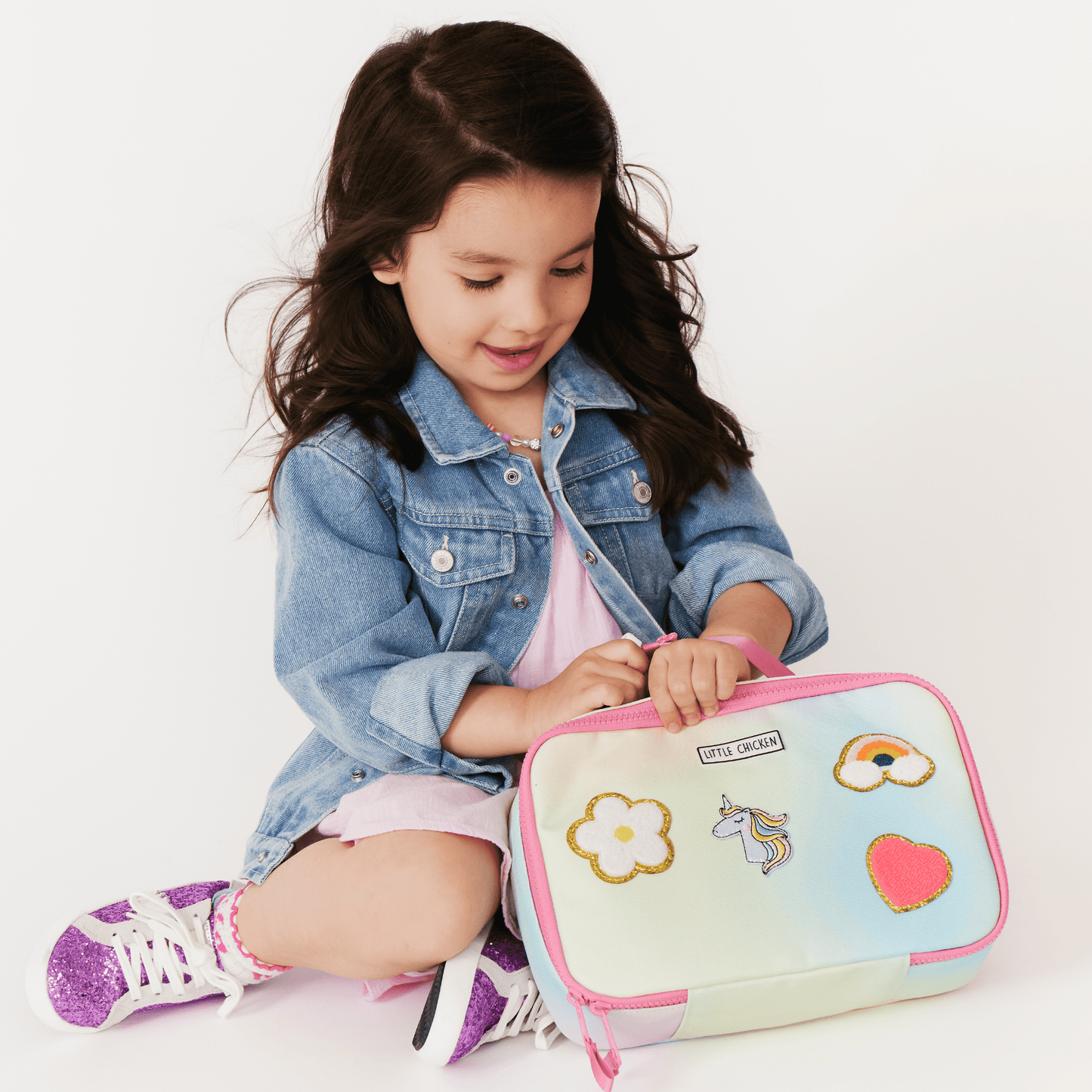 Young girl sitting on the floor with a colorful lunch bag featuring cartoon designs.