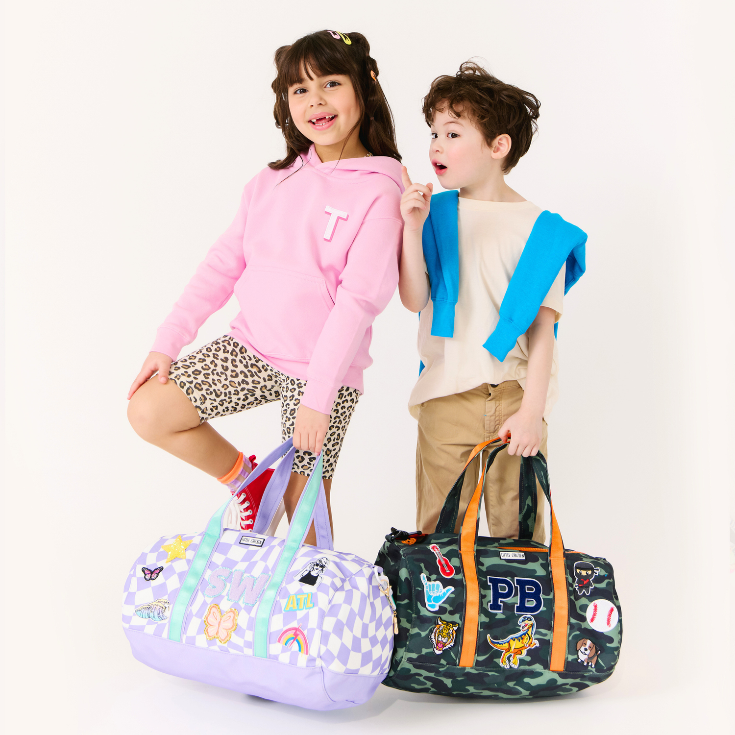 Boy and girl holding personalized kids duffle bags with custom patches and embroidered initials — purple checker and camo designs for boys and girls