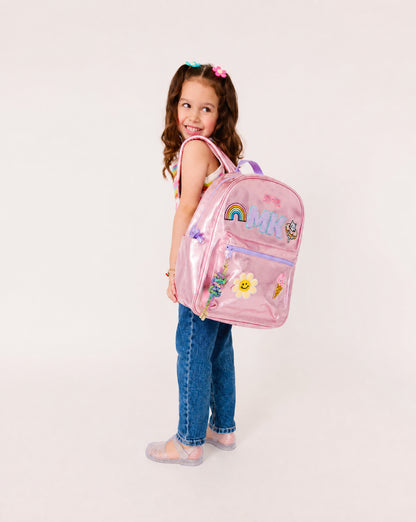 Young girl wearing a personalized metallic pink backpack with custom initials and colorful patches. Perfect for school, camp, travel and back-to-school adventures.
