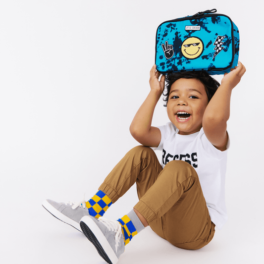 Child holding a blue lunch bag with smiley face design on a white background