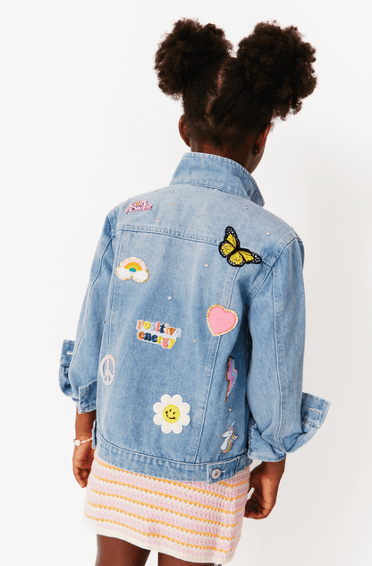A girl facing away from the camera wears a light wash denim jacket with colorful patches and sequin details.