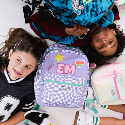 Two children with backpacks, one purple with 'EM' and a star, the other pink with a guitar design.
