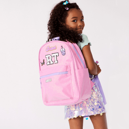 Young girl wearing a pink backpack with decorative elements on a white background
