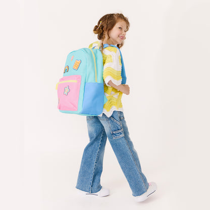 Young girl wearing a pastel blue and pink backpack featuring rainbow, heart and star patches.