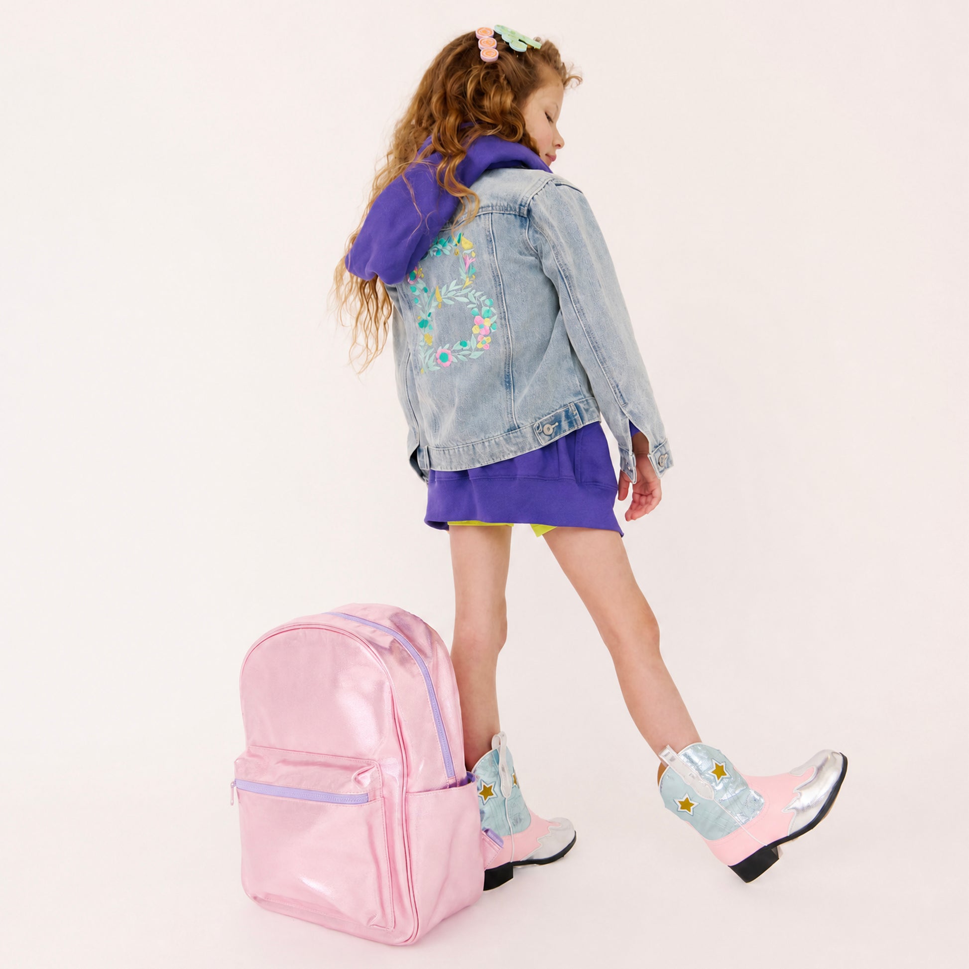 Child wearing a denim jacket with a pink metallic back on a white backpack