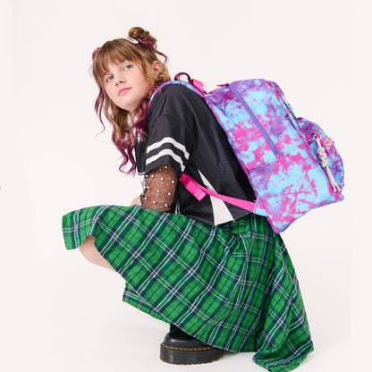 girl wearing a tie dye backpack and green plaid skirt on a white background