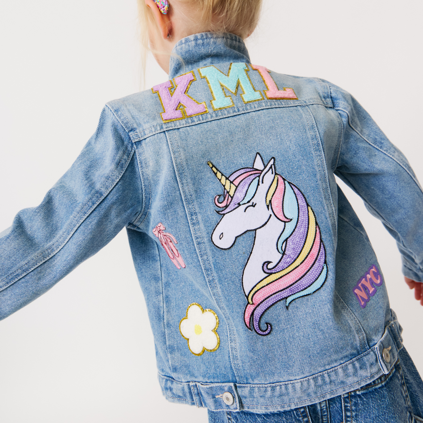 a girl wearing a customized denim jacket with various colorful patches on it. The jacket is adorned with different designs and monogrammed