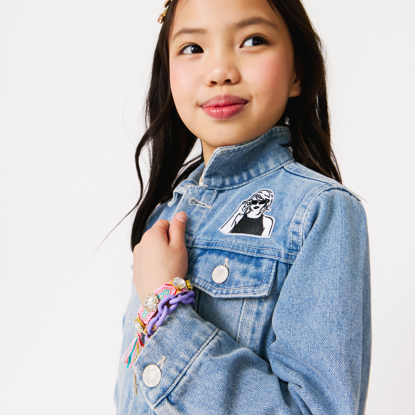 Young girl wearing a denim jacket with a taylor swift patch on a white background