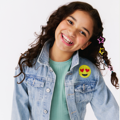 Young girl wearing a denim jacket with emoji patches on a white background