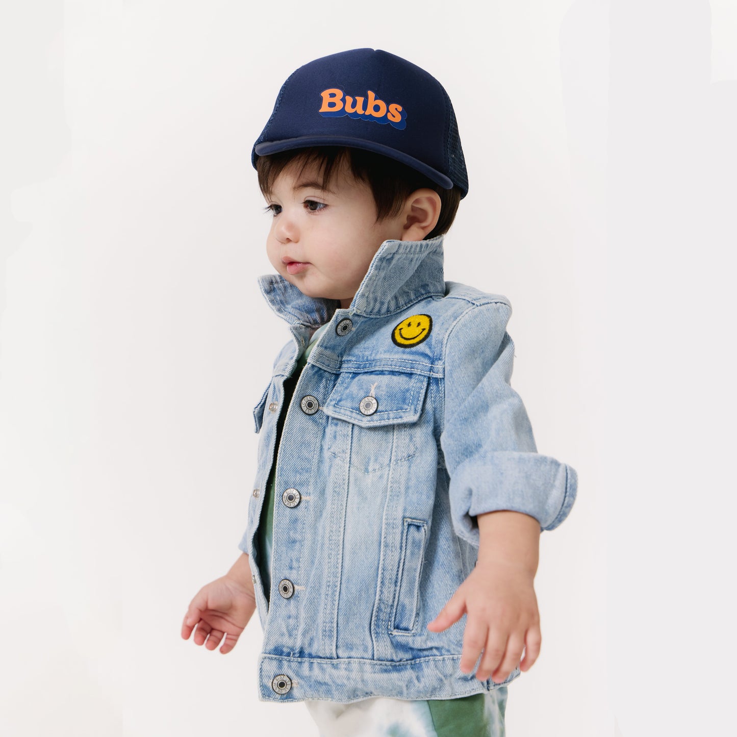 Child wearing a denim jacket and navy cap with 'Bubs' text on a white background