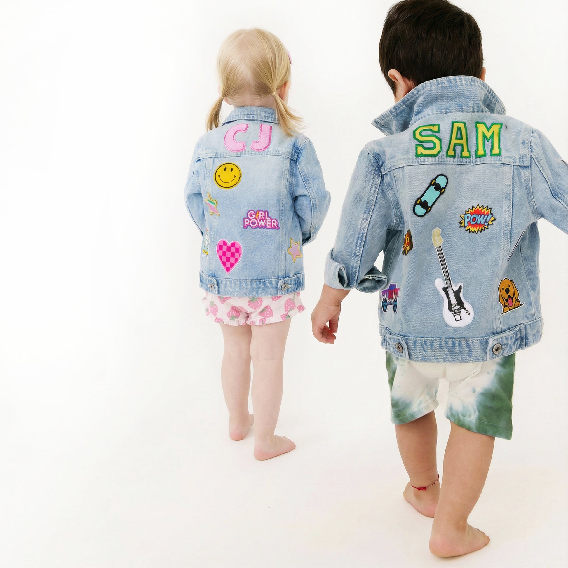 Two children wearing denim jackets with various patches on a white background