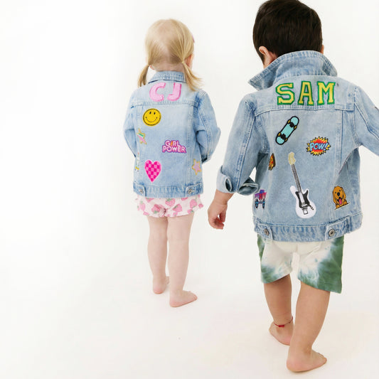 Two children wearing denim jackets with various patches on a white background