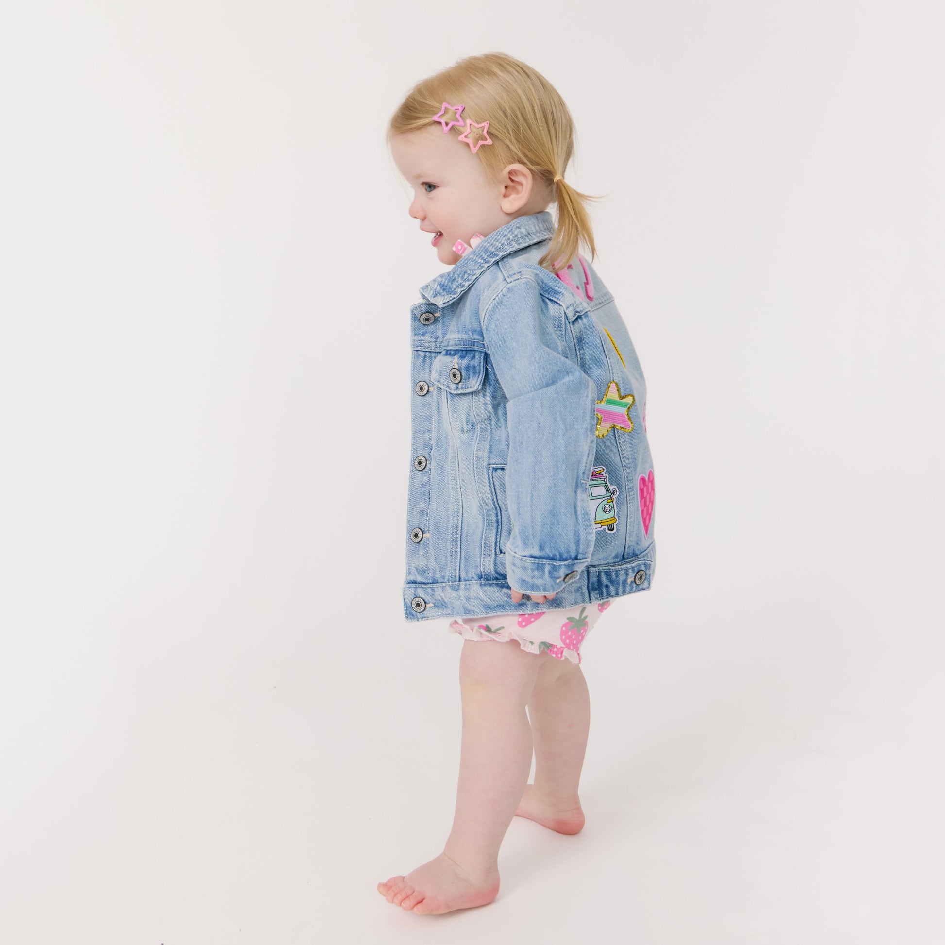 Child wearing a denim jacket with colorful patches on a white background