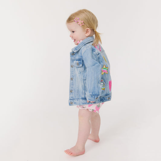 Child wearing a denim jacket with colorful patches on a white background