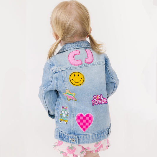 Child wearing a denim jacket with colorful patches on a white background
