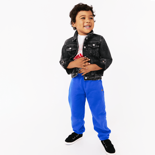 Child wearing a black denim jacket, white shirt with red design, and blue pants on a white background