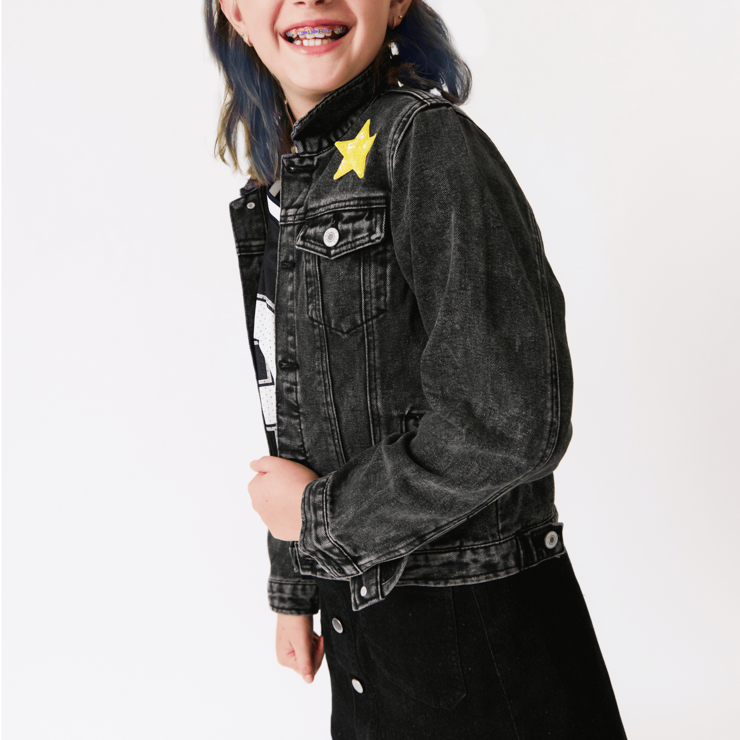 A girl wearing a black denim jacket with a yellow star patch on a white background