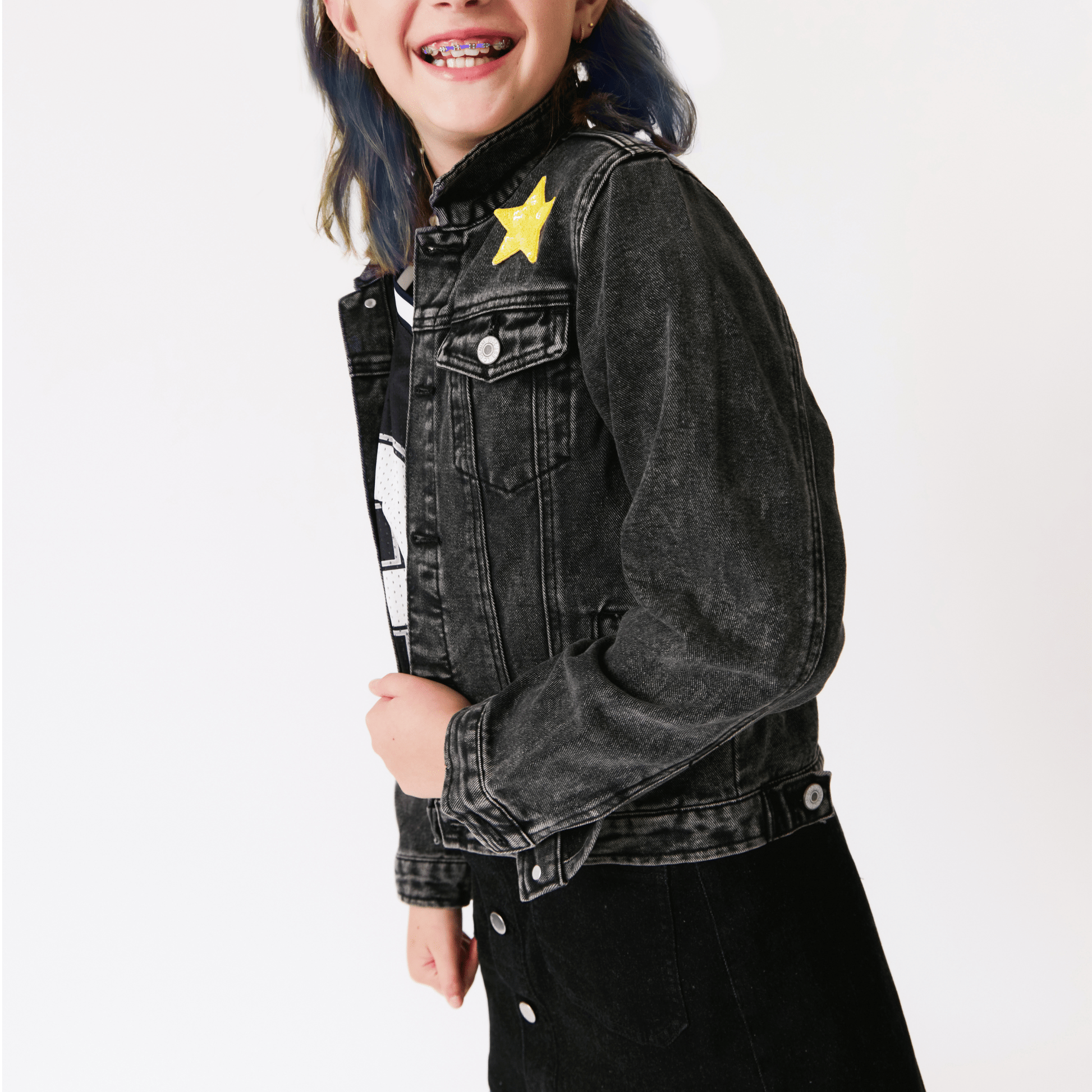 A girl wearing a black denim jacket with a yellow star patch on a white background