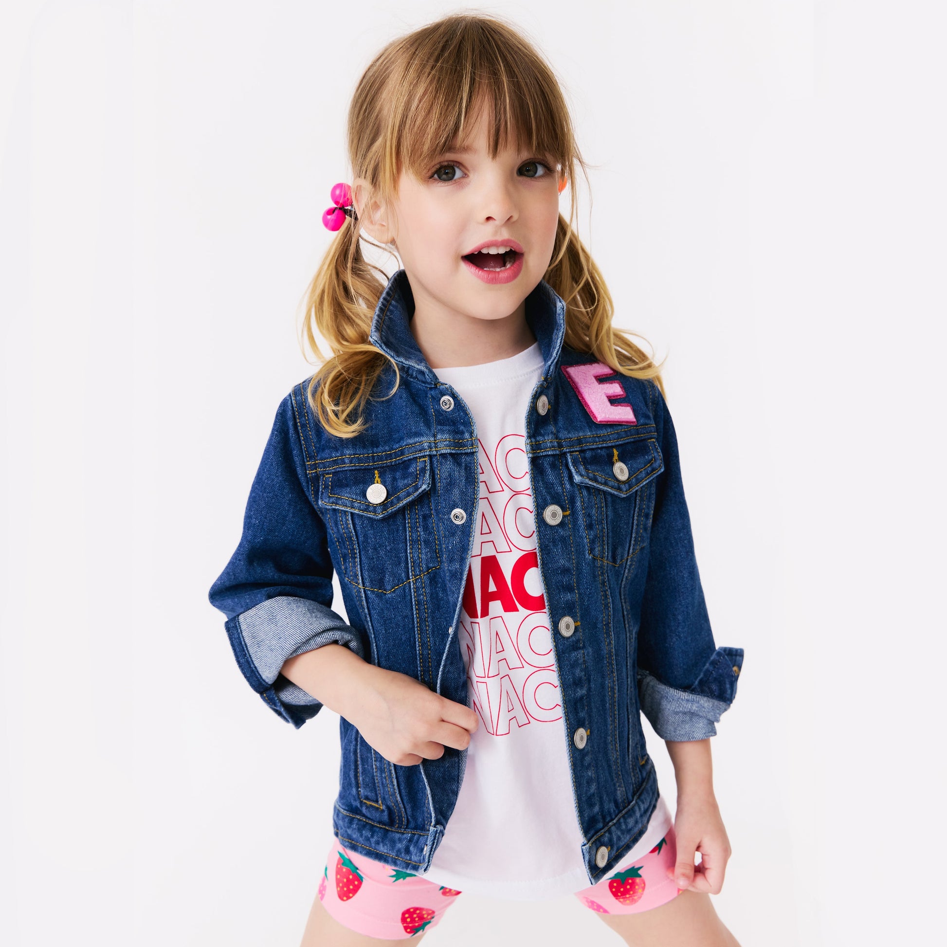 Young girl wearing a denim jacket with pink letters on a white background