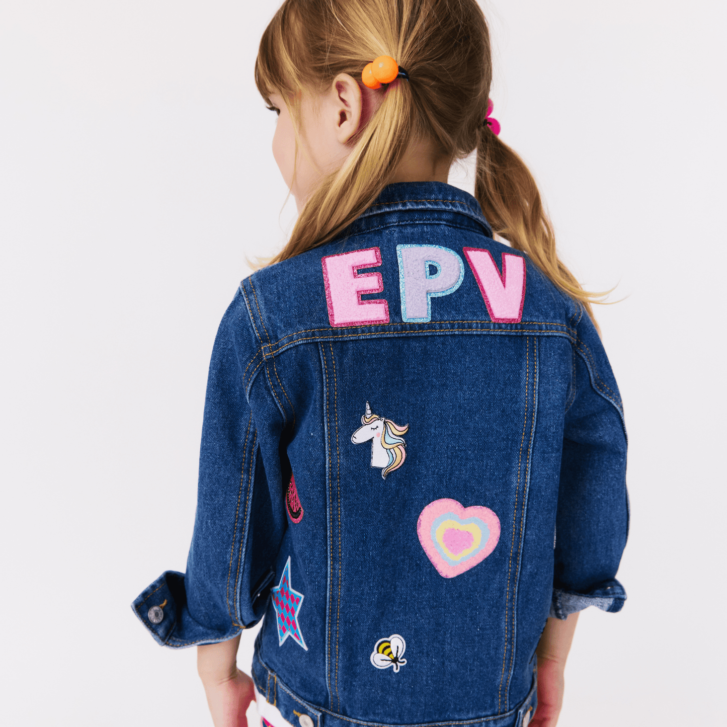 Child wearing a custom denim jacket with colorful patches and  initials on a white background