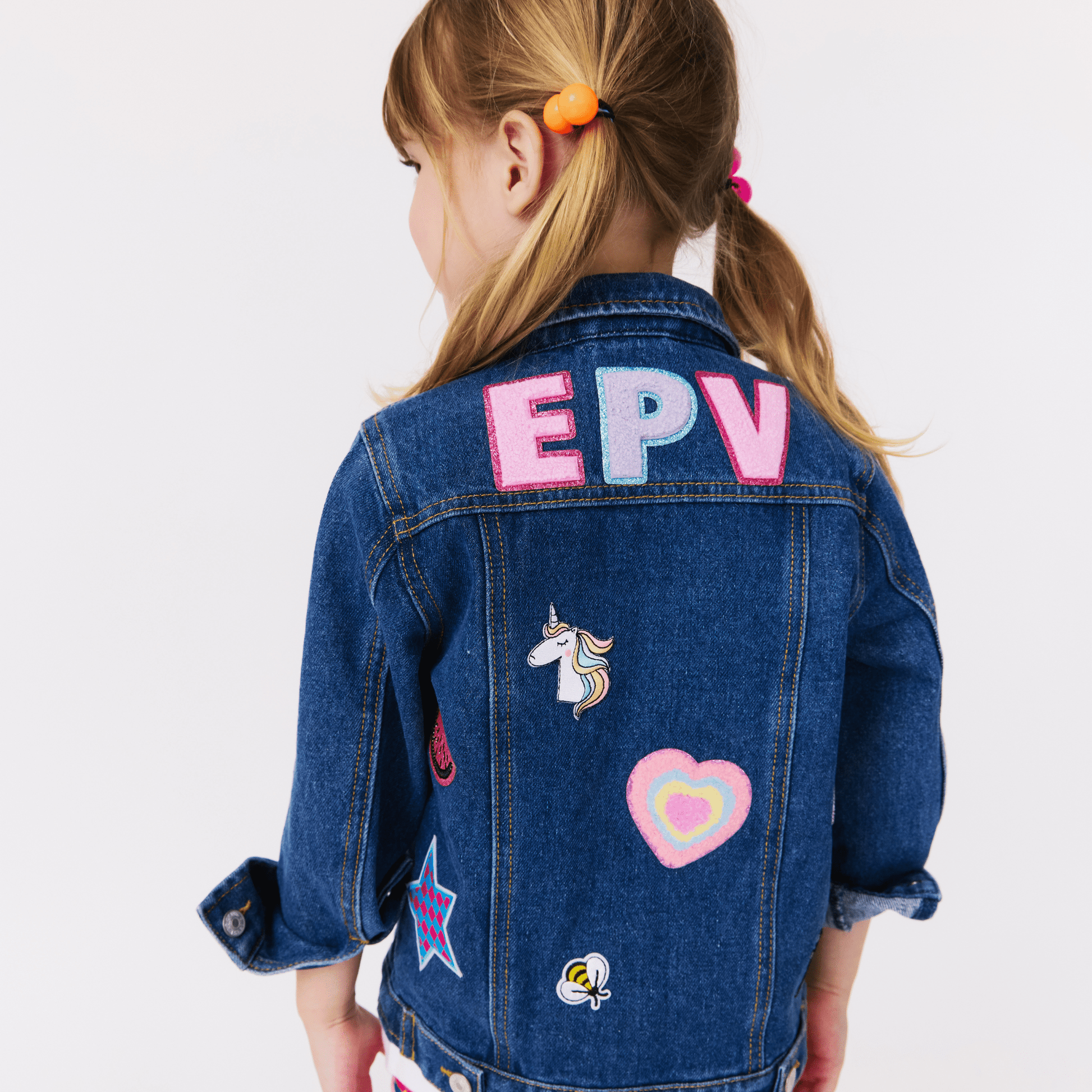 Child wearing a custom denim jacket with colorful patches and  initials on a white background