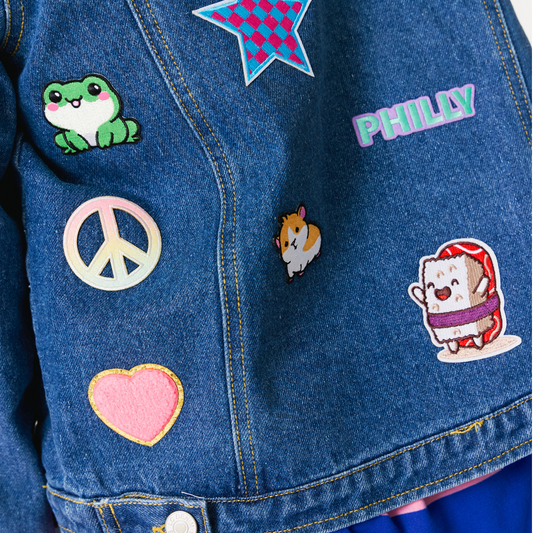 Blue denim jacket with various patches including a frog, philly, peace sign, heart, and cartoon character.