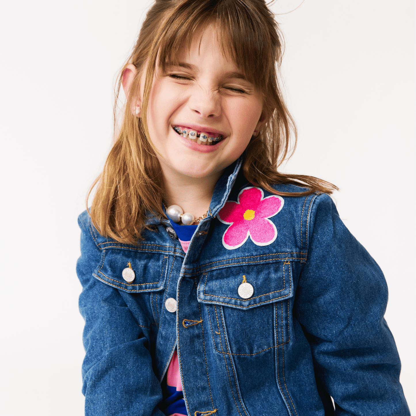 Young girl wearing a denim jacket with a pink flower patch on a white background