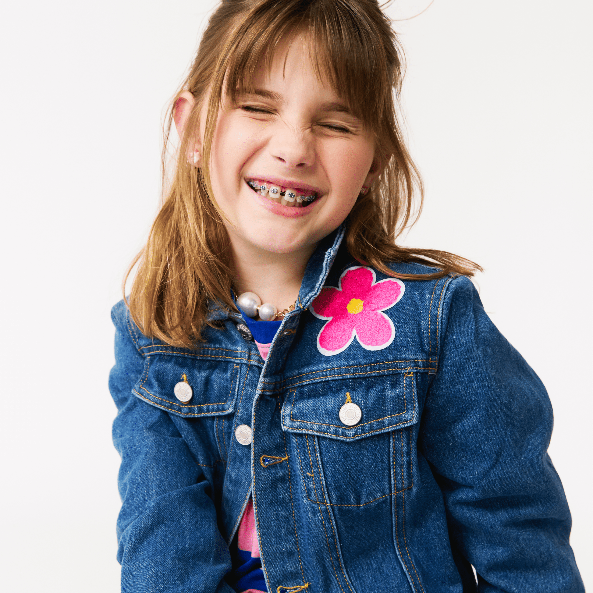 Young girl wearing a denim jacket with a pink flower patch on a white background
