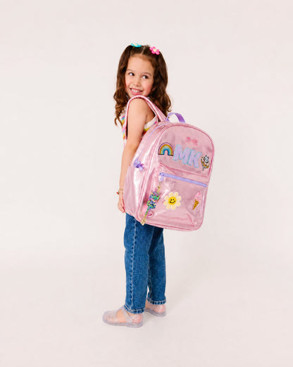 Young girl wearing a personalized metallic pink backpack with custom initials and colorful patches. Perfect for school, camp, travel and back-to-school adventures.
