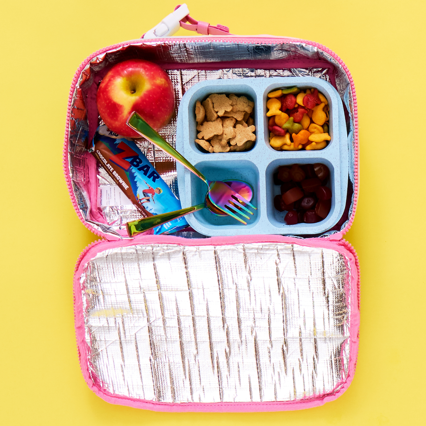 Open lunch box with compartments filled with snacks on a yellow background