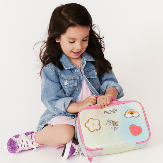 Young girl sitting on the floor with a colorful lunch bag featuring cartoon designs.