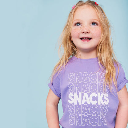 A purple kids' t-shirt with the word 'SNACKS' printed in red letters multiple times.